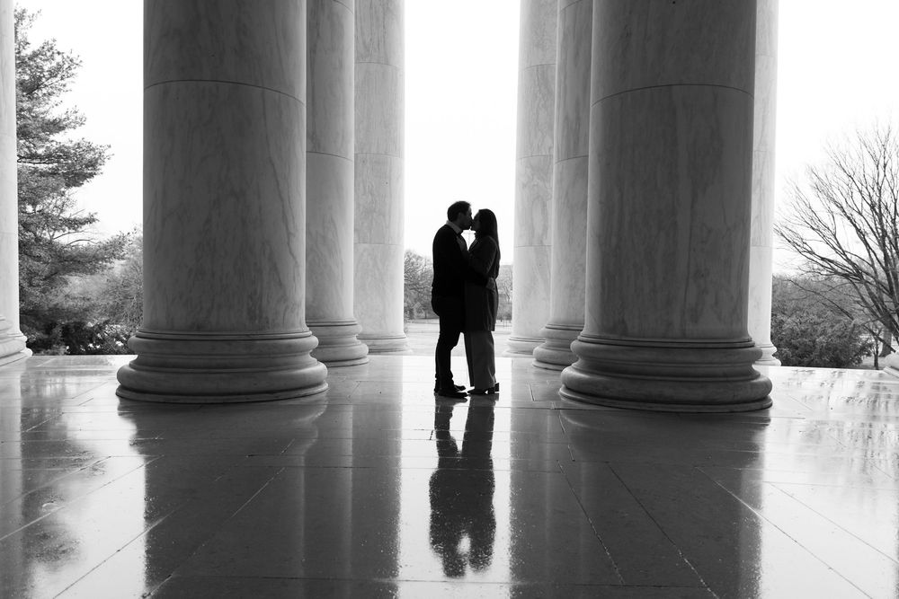 Black and white photo of a couple silhouetted kissing between marble columns at the Jefferson Memorial.