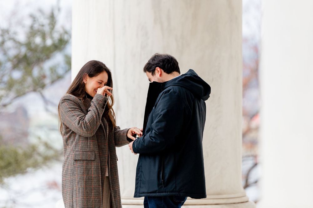Man proposes to emotional woman near white columns outdoors in winter, romantic marriage proposal moment.