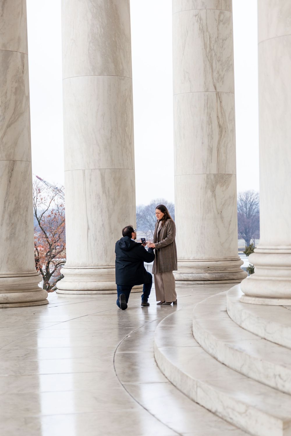 Man proposes on one knee to woman among marble columns at Jefferson Memorial in Washington DC.