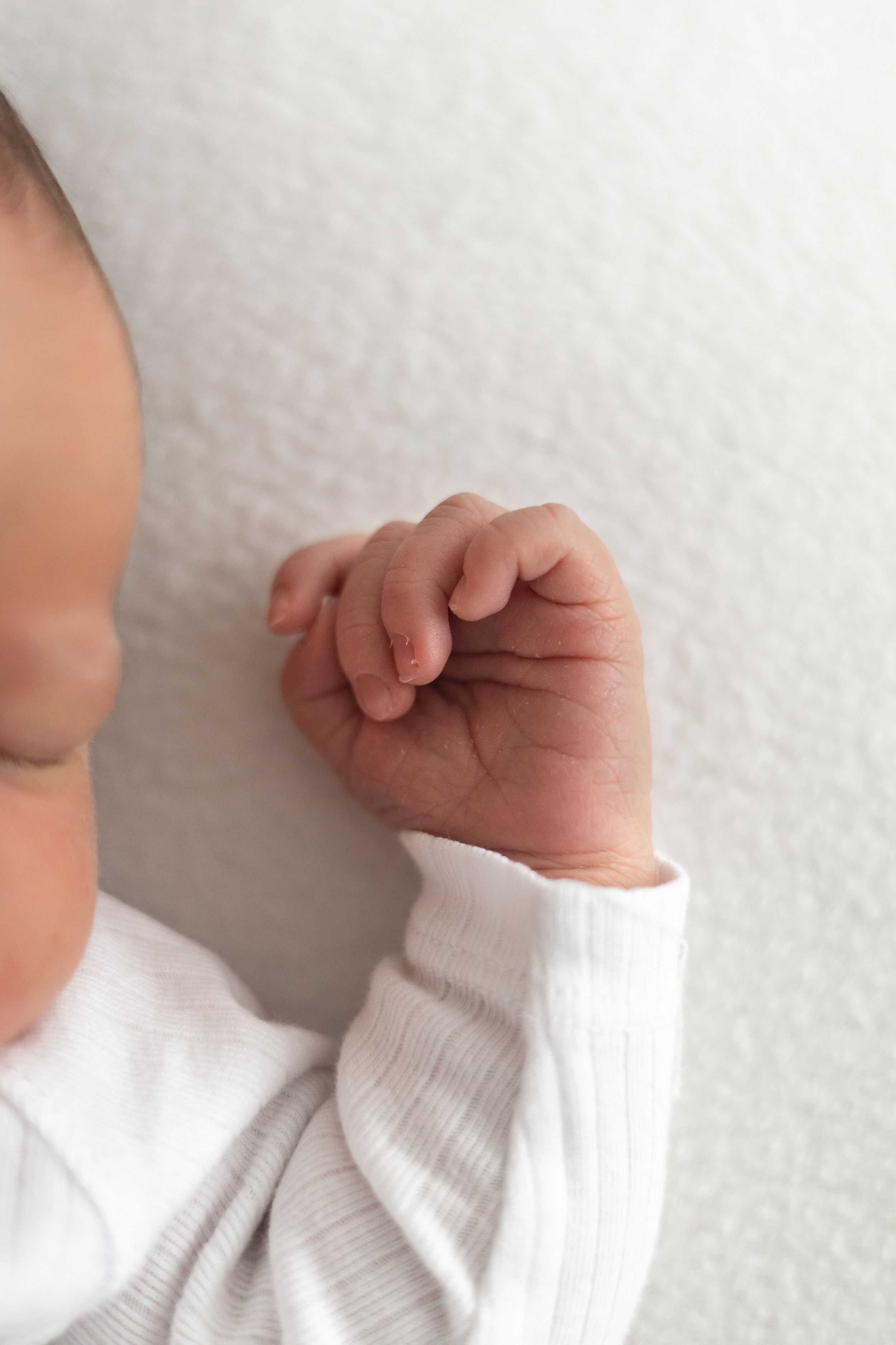 Close-up of a sleeping newborn baby's tiny clenched fist in a white striped onesie natural newborn photography Nottingham