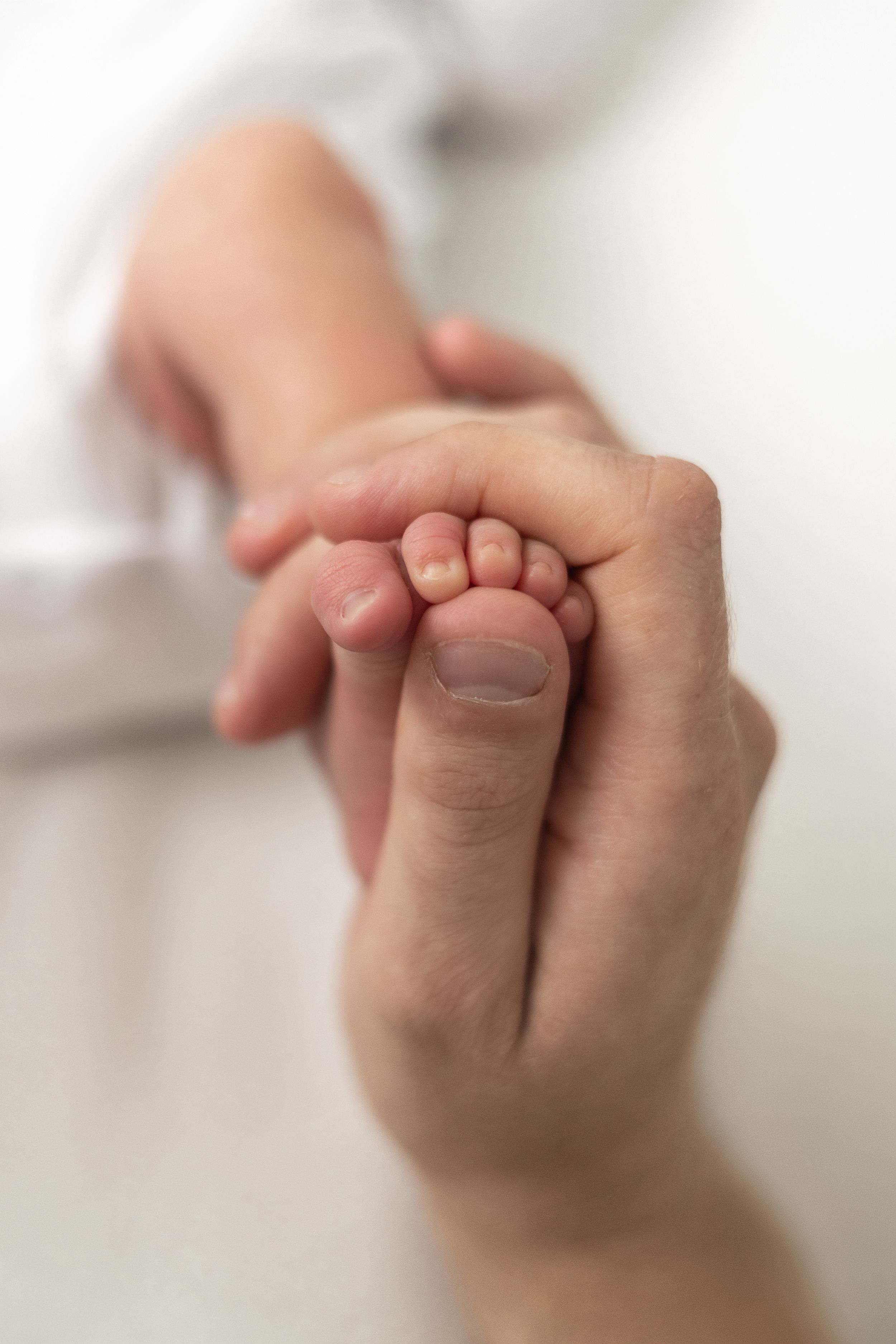 Close-up of dad's hand gently holding his tiny newborns baby foot, natural newborn photography Nottingham