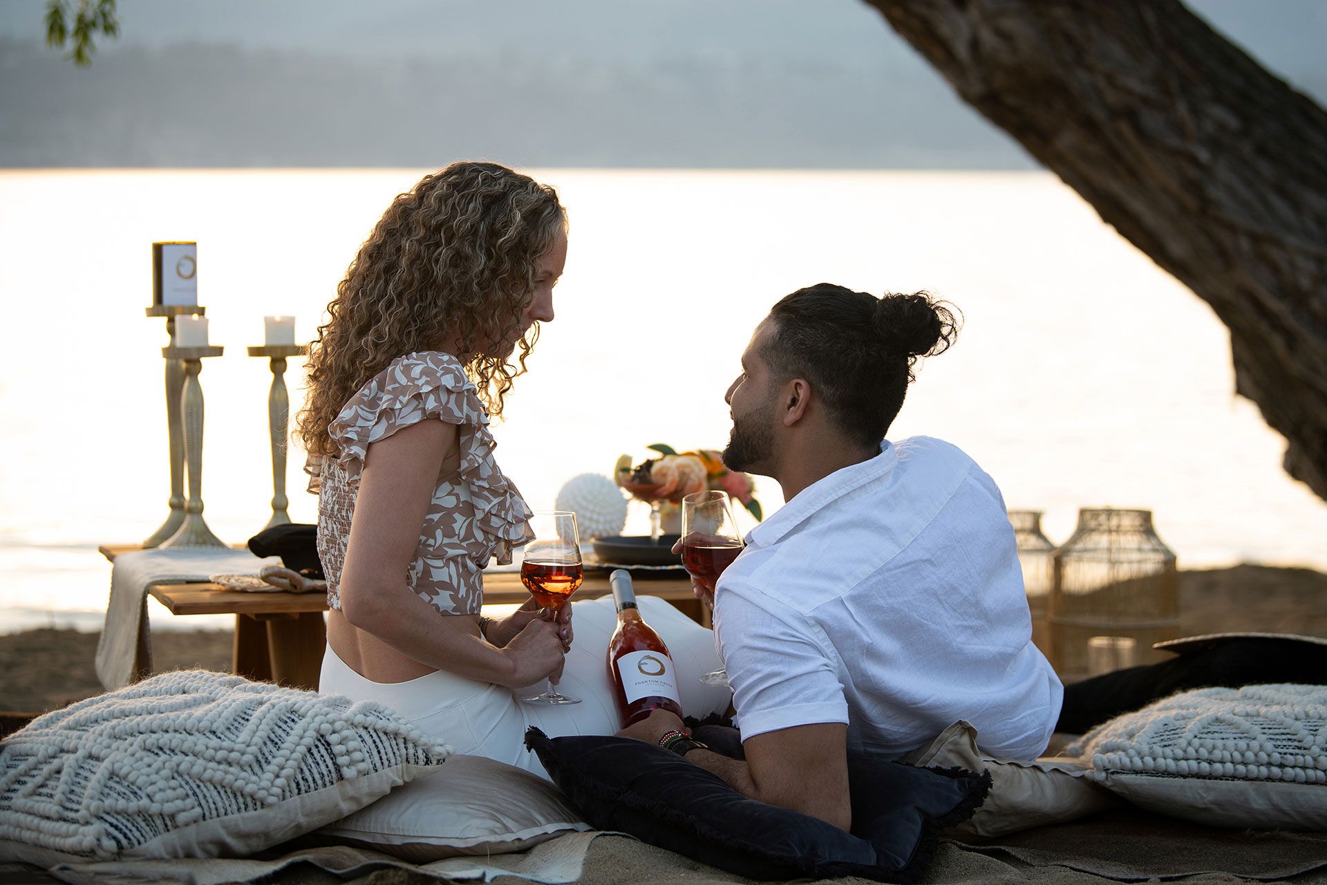 Woman in red top pouring white wine at outdoor restaurant table with food and wine glasses.
