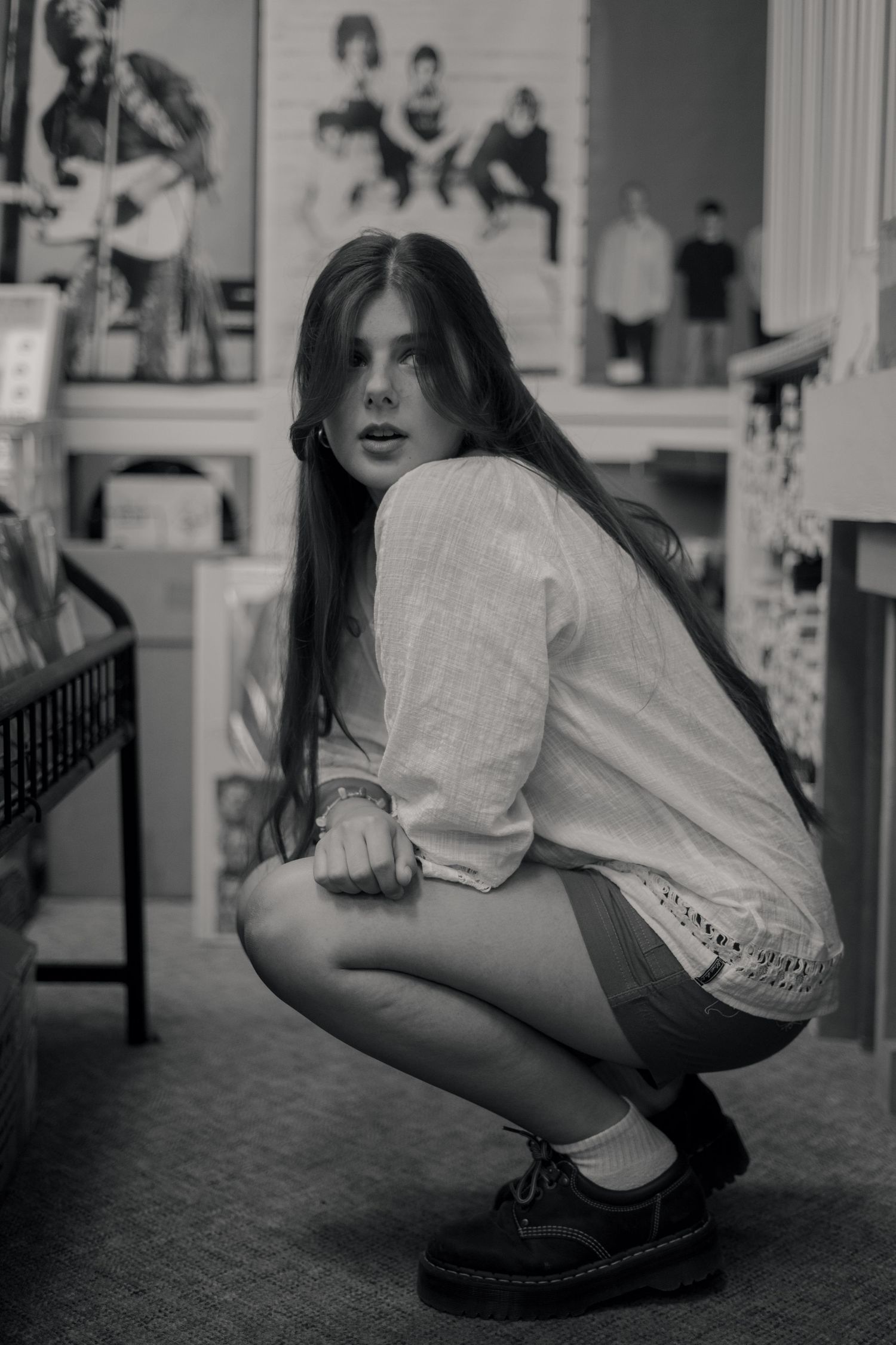 Young woman crouching in a store, wearing a white top and shorts, captured in black and white photography.