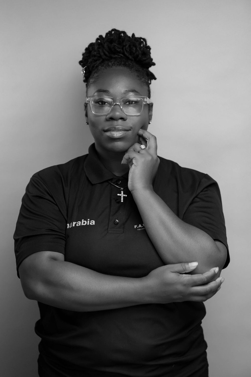 Black and white portrait of a woman in a black polo shirt with glasses, posing thoughtfully with hand on chin.