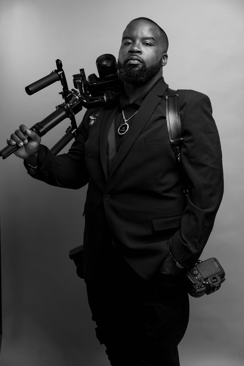 Black and white portrait of a bearded man in a suit holding a professional camera rig on his shoulder.