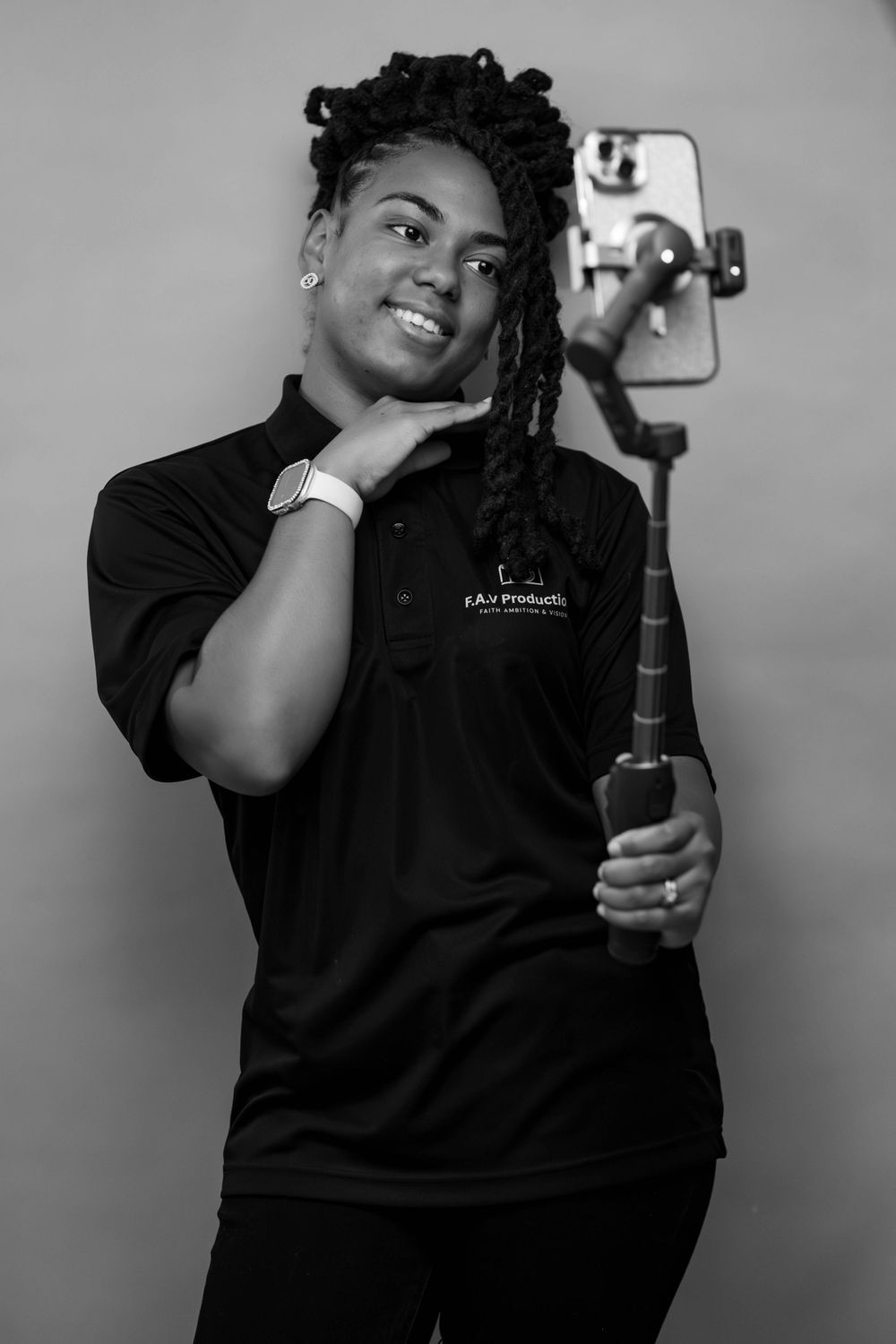 Black and white portrait of a smiling woman holding a gimbal stabilizer with smartphone, wearing a branded polo shirt.