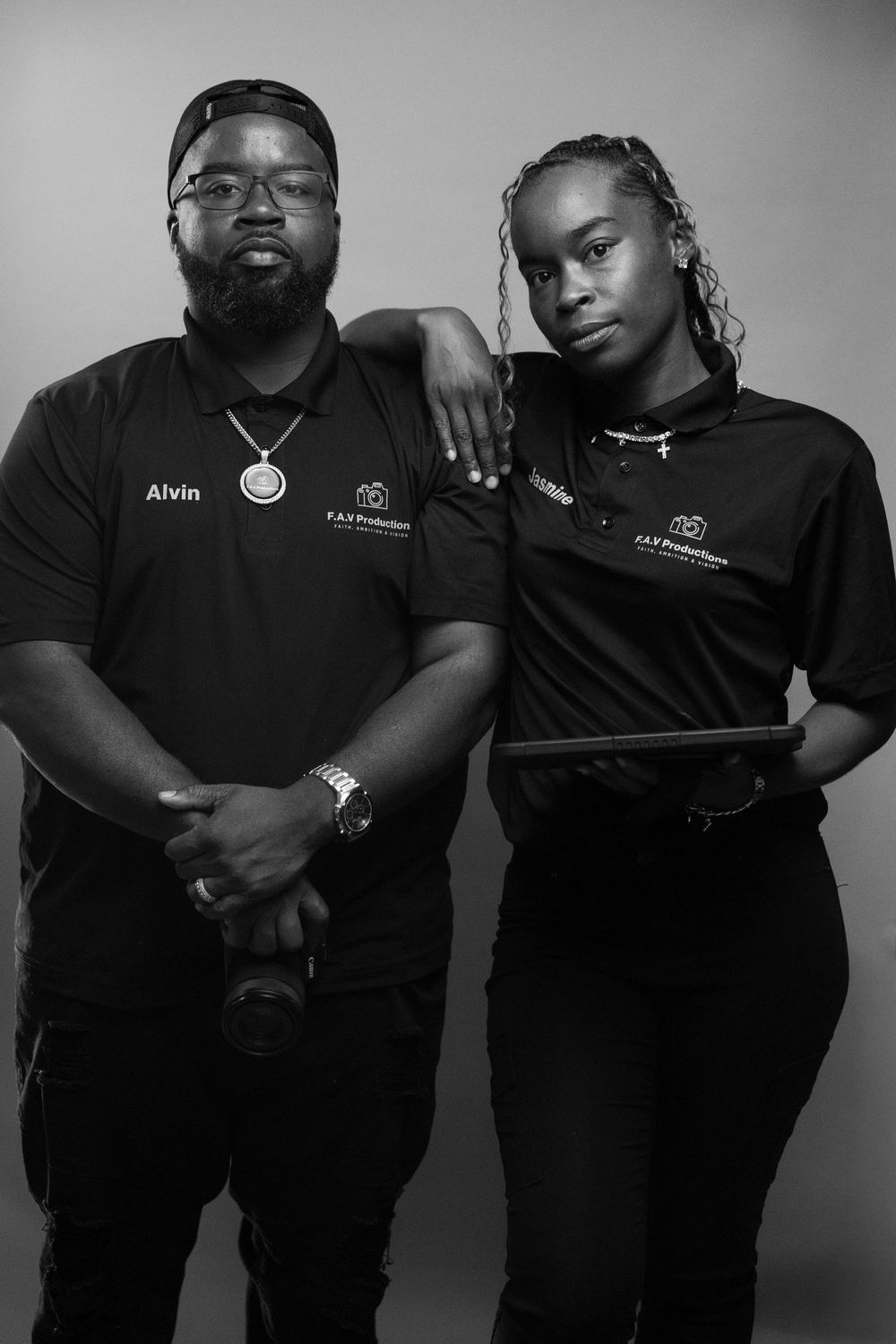 Black and white portrait of two professionals in matching F.A.S Productions shirts, one holding a tablet.