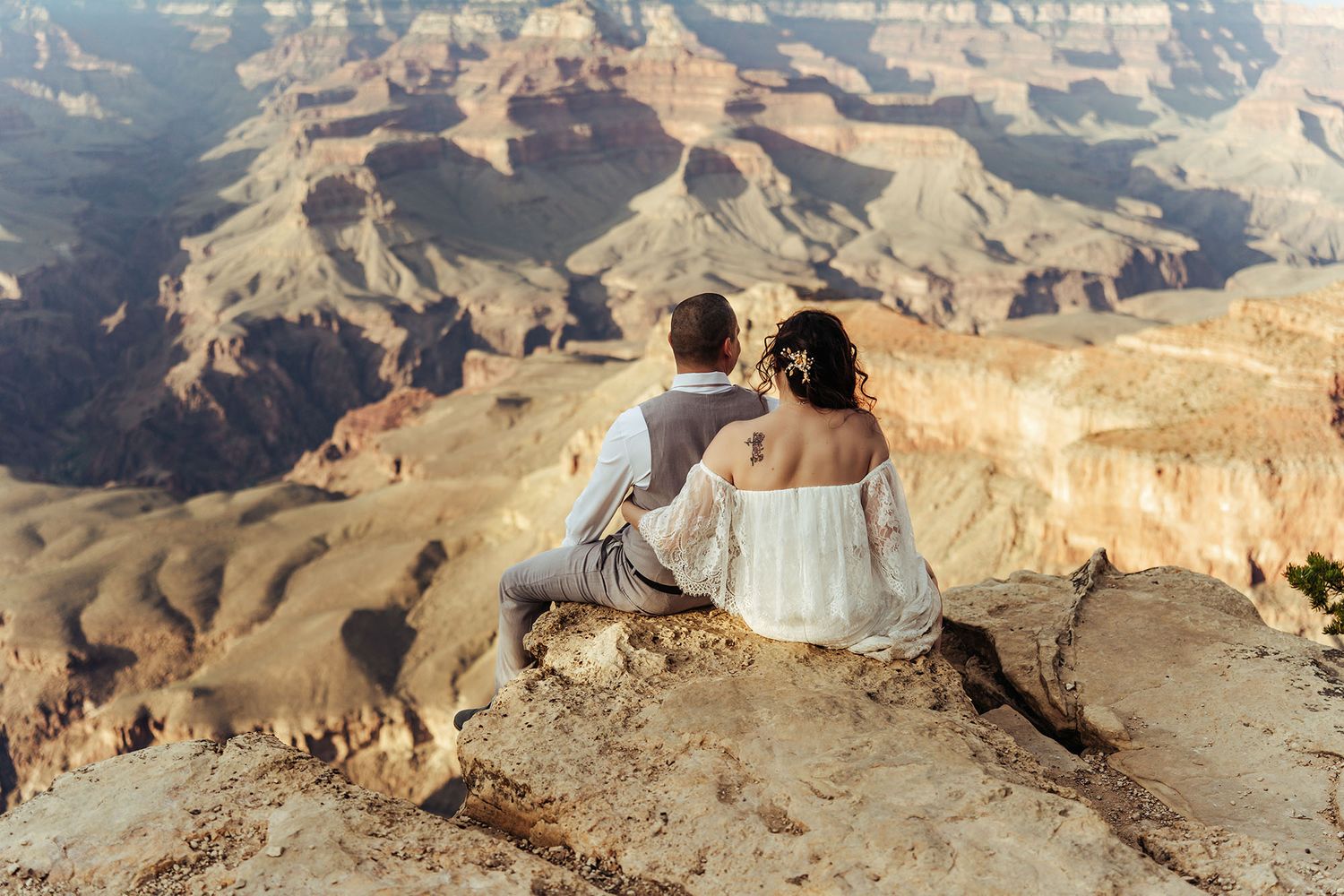 Couple poses in Sedona Arizona desert landscape at sunset, bride in white gown holding bouquet, groom in navy suit.