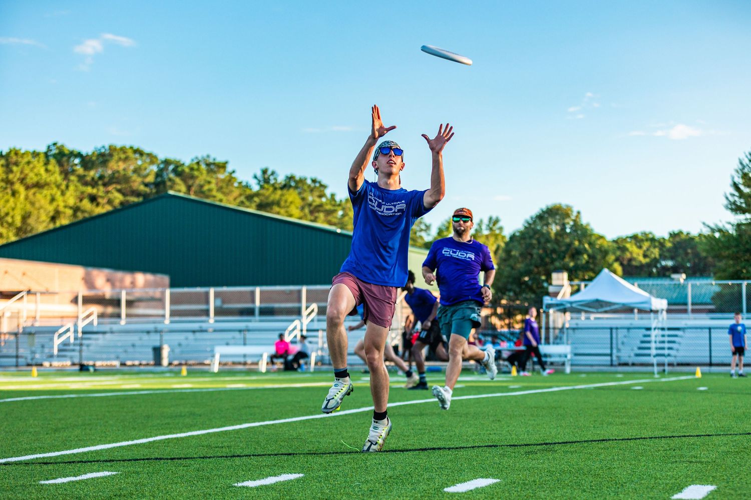 Player in blue jersey leaps to catch a flying disc on a green turf field during an ultimate frisbee game.
