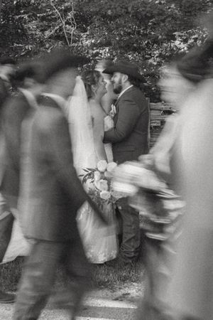 Black and white wedding photo of bride and groom kissing while guests walk past in motion blur.
