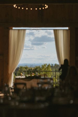 Elegant wedding reception venue with sheer white curtains framing a scenic countryside view under a cloudy sky.