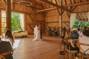 Couple sharing first dance in rustic wooden barn wedding venue with string lights and guests seated on cross-back chairs.