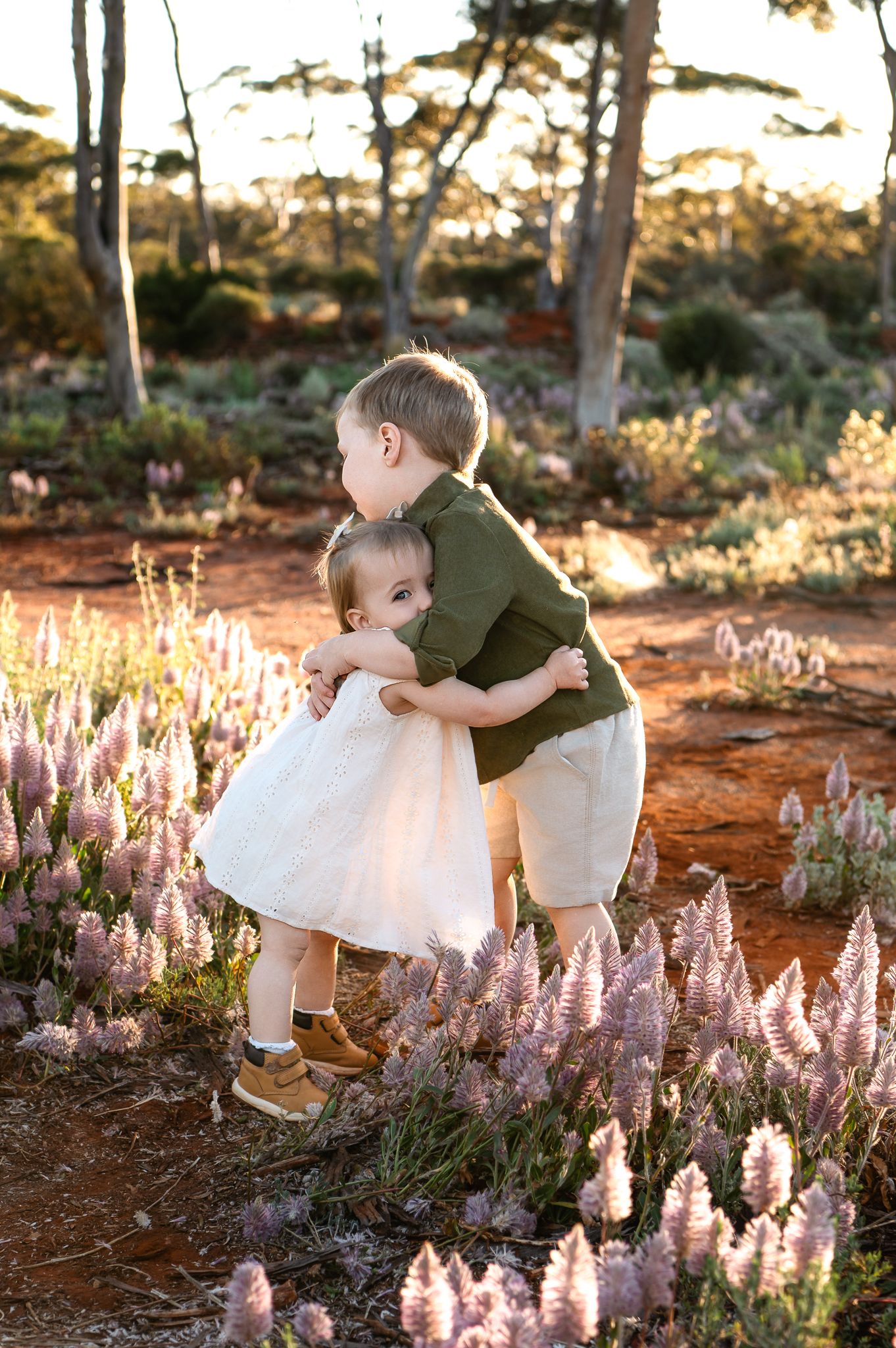 Happy Asian family of three posing outdoors in golden hour light among desert shrubs, parents holding toddler daughter.