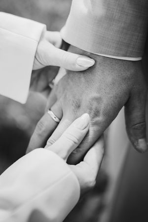 Black and white close-up of the bride's manicured hands gently touching the groom's hand and wedding ring.