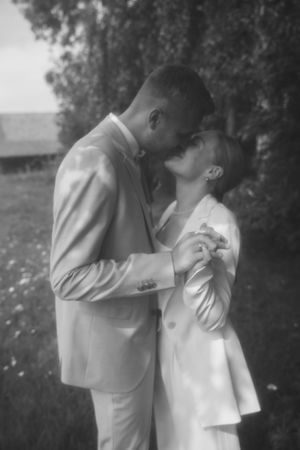 Black and white photo of a couple kissing in a sunlit garden, holding hands in wedding attire.