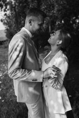 Black and white portrait of a bride and groom gazing at each other and holding hands under soft dappled light.