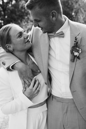 Black and white wedding portrait of a bride and groom embracing, the groom wearing a bow tie and floral boutonniere.