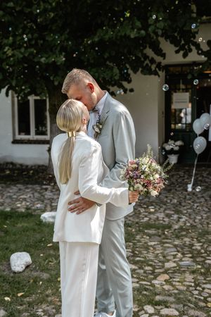 Brautpaar umarmt sich in einem gepflasterten Innenhof, umgeben von Seifenblasen, während die Braut ihren Brautstrauß hält.