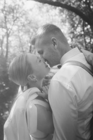 A black and white close-up of a bride and groom sharing a tender nose-to-nose moment among softly lit trees.