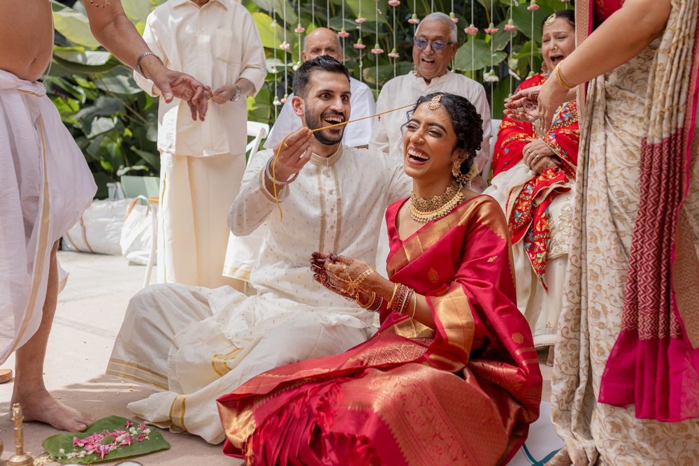 Joyful couple in traditional Indian wedding attire laughing during a Hindu ceremony outdoors.