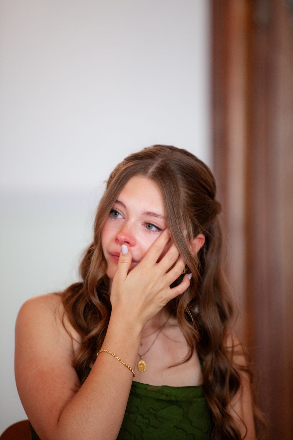 Emotional young woman in green dress with wavy hair wiping tears at a wedding celebration.