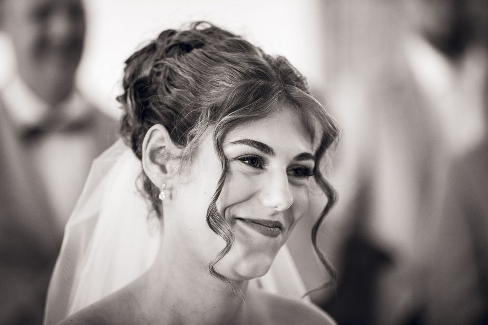 Black and white portrait of a smiling bride wearing a veil and elegant updo hairstyle on her wedding day.