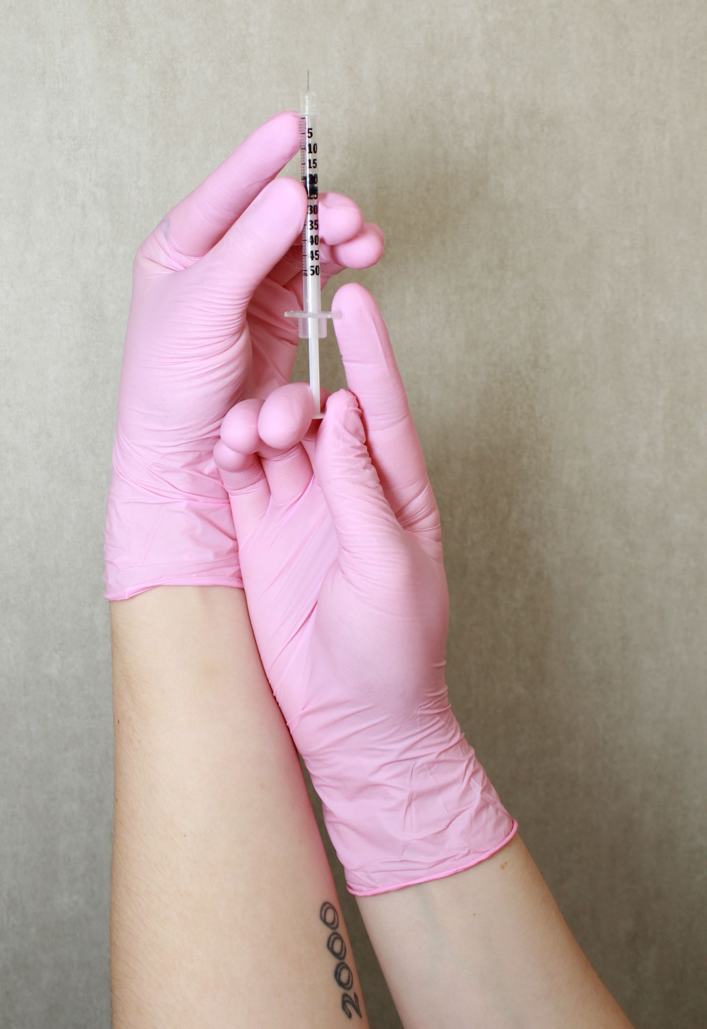 Hands in pink nitrile gloves holding a medical syringe, preparing for a cosmetic injection procedure.