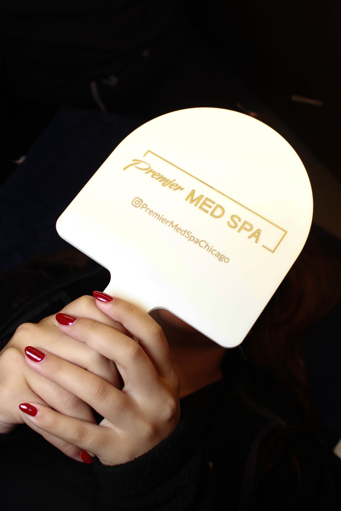 Person holding a glowing Premier Med Spa branded paddle sign with red manicured nails, Chicago med spa.