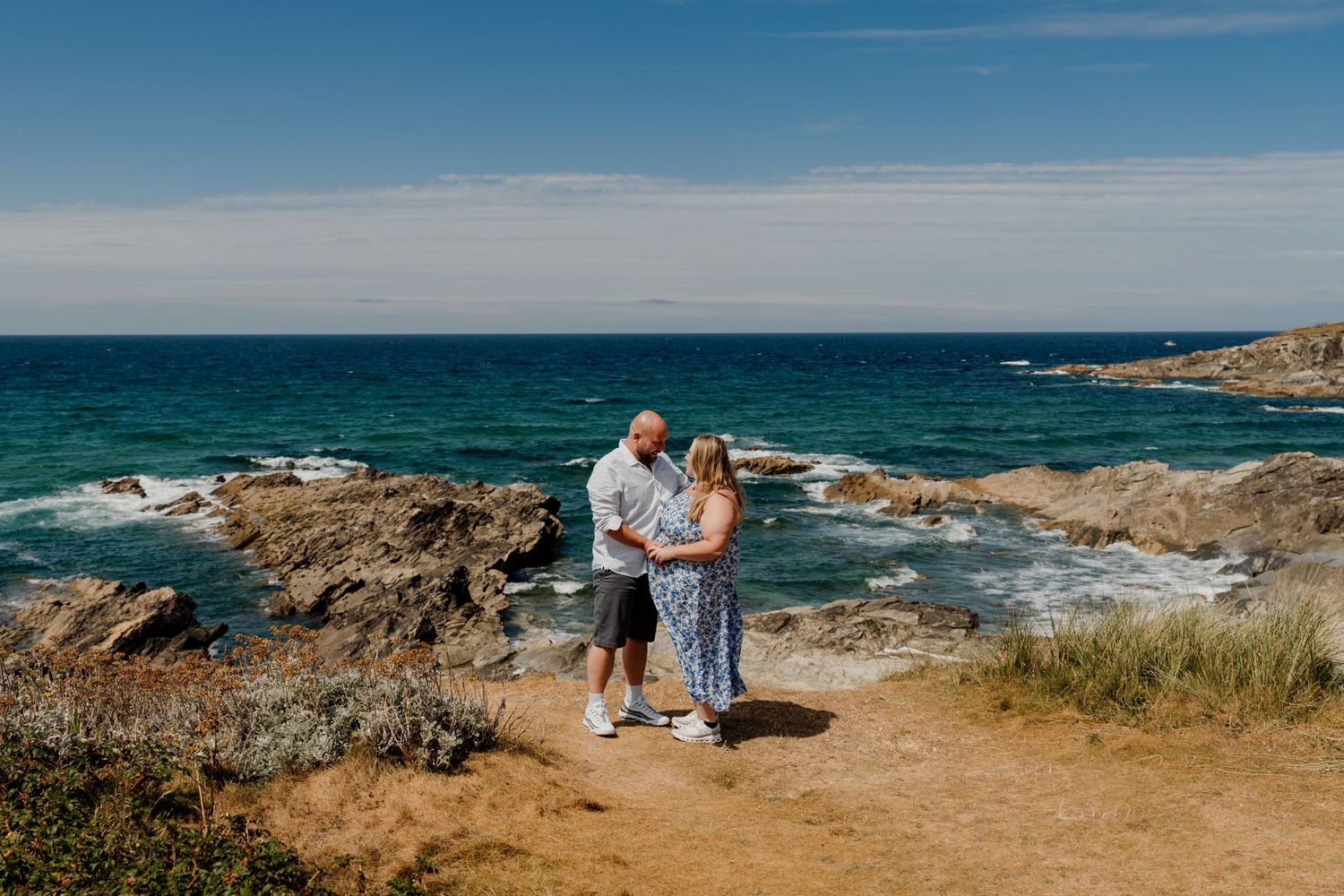Couple holding hands during engagement photoshoot by the headland hotel overlooking little fistral beach