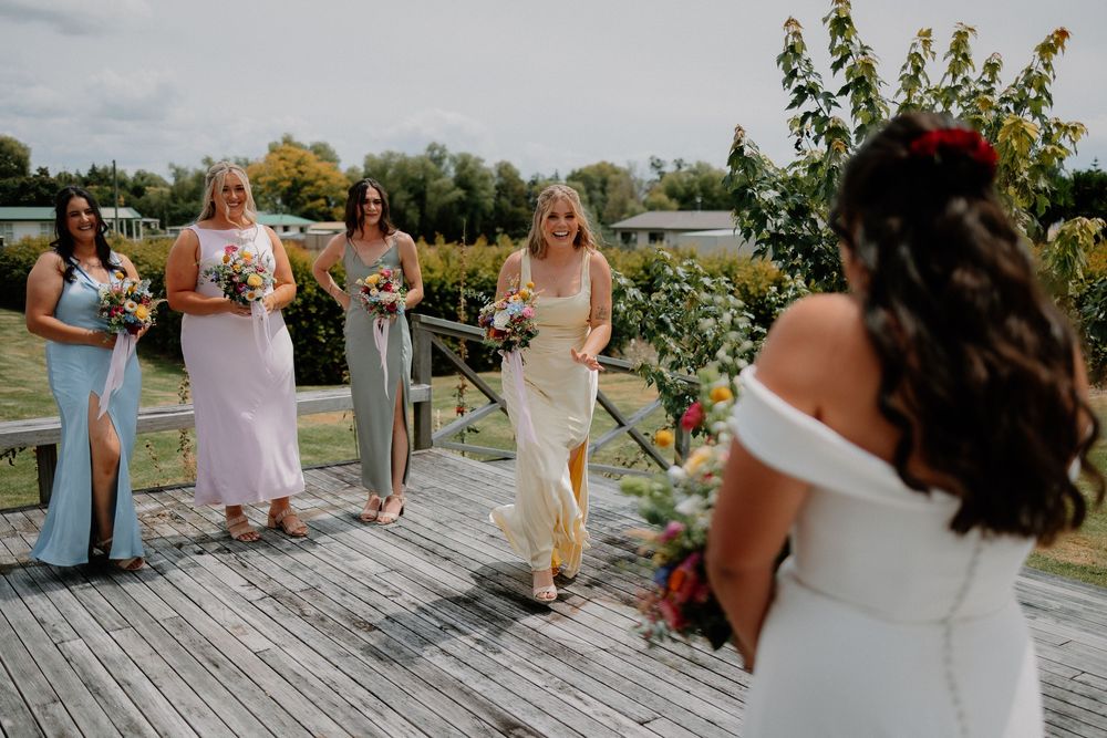 Wedding party members dance and celebrate together on a rustic wooden deck during an outdoor reception.