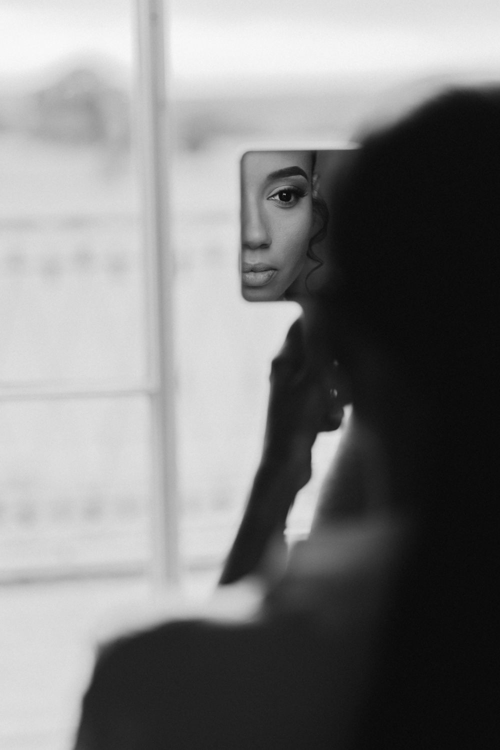 An artistic black and white portrait captured through a small mirror reflection.
