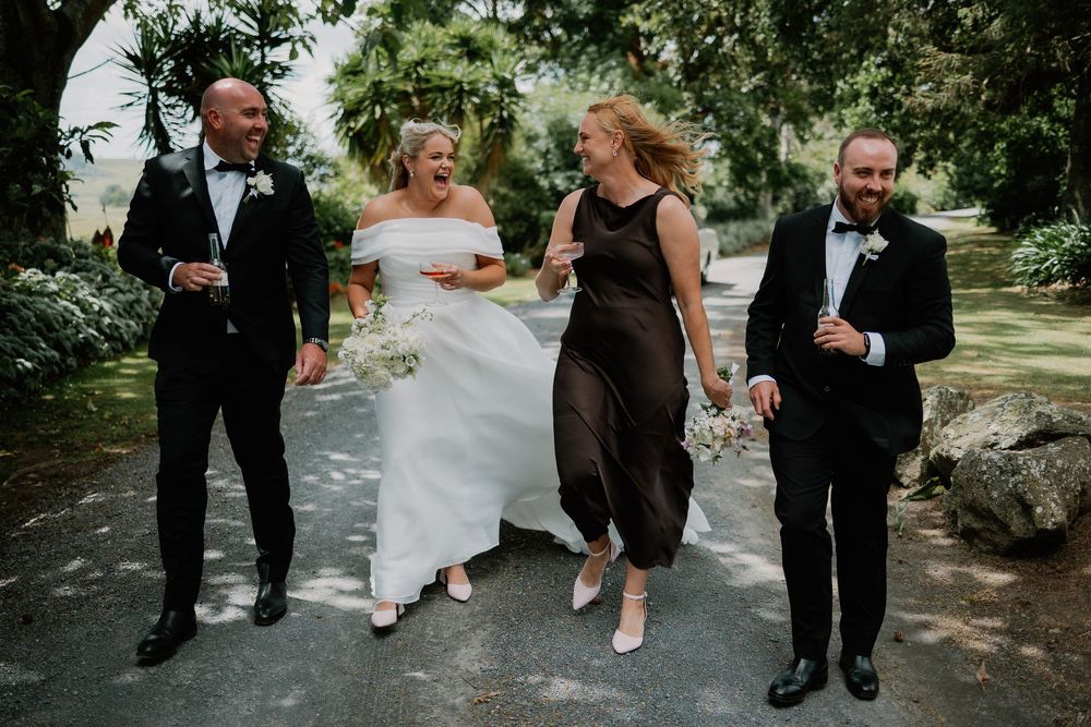 Wedding party members sit casually on stone steps in a garden setting, creating a relaxed group photo moment.