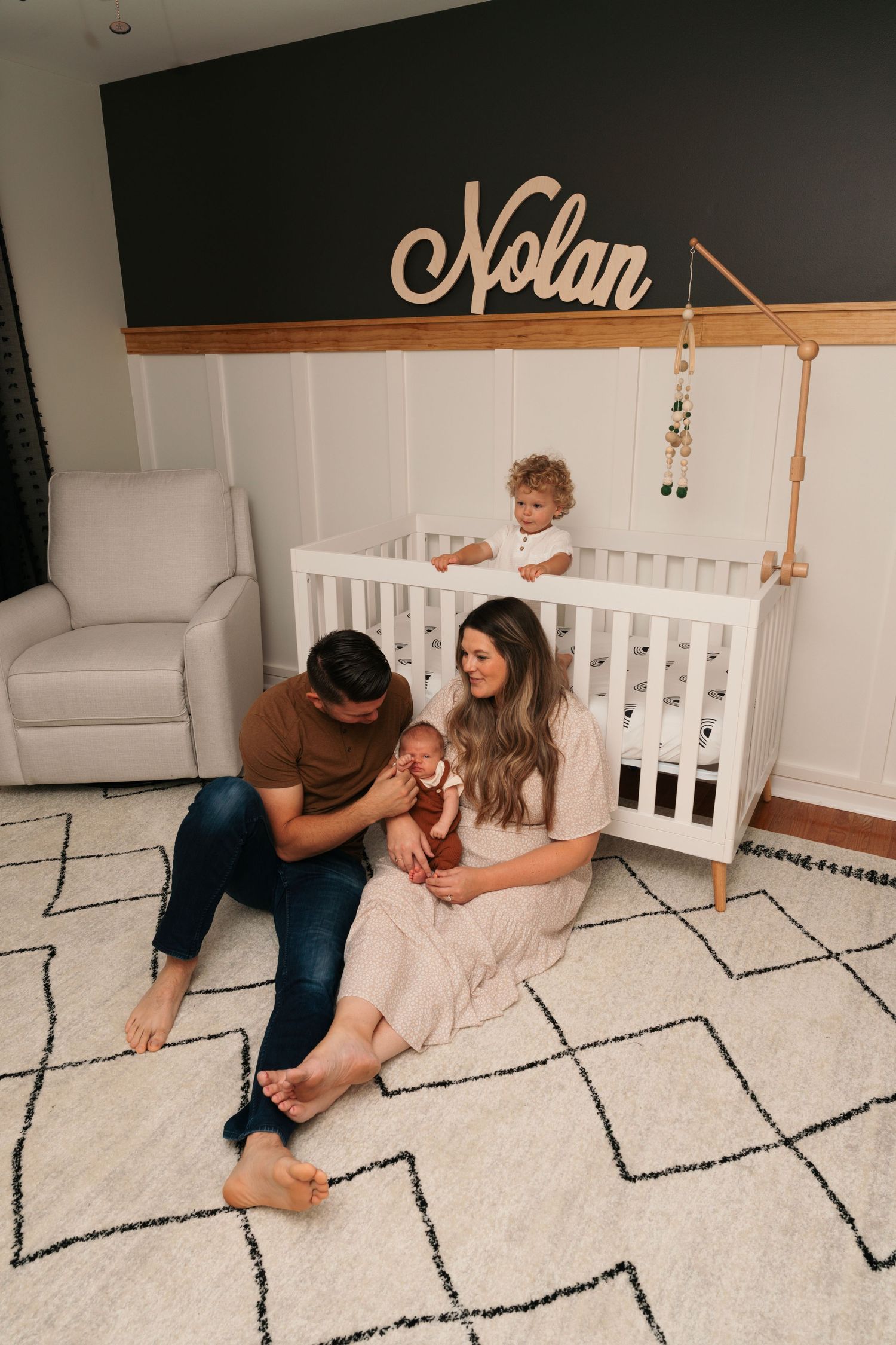 Family sitting on geometric patterned rug in nursery with name 'Nolan' on wall. In home photography Chicago.
