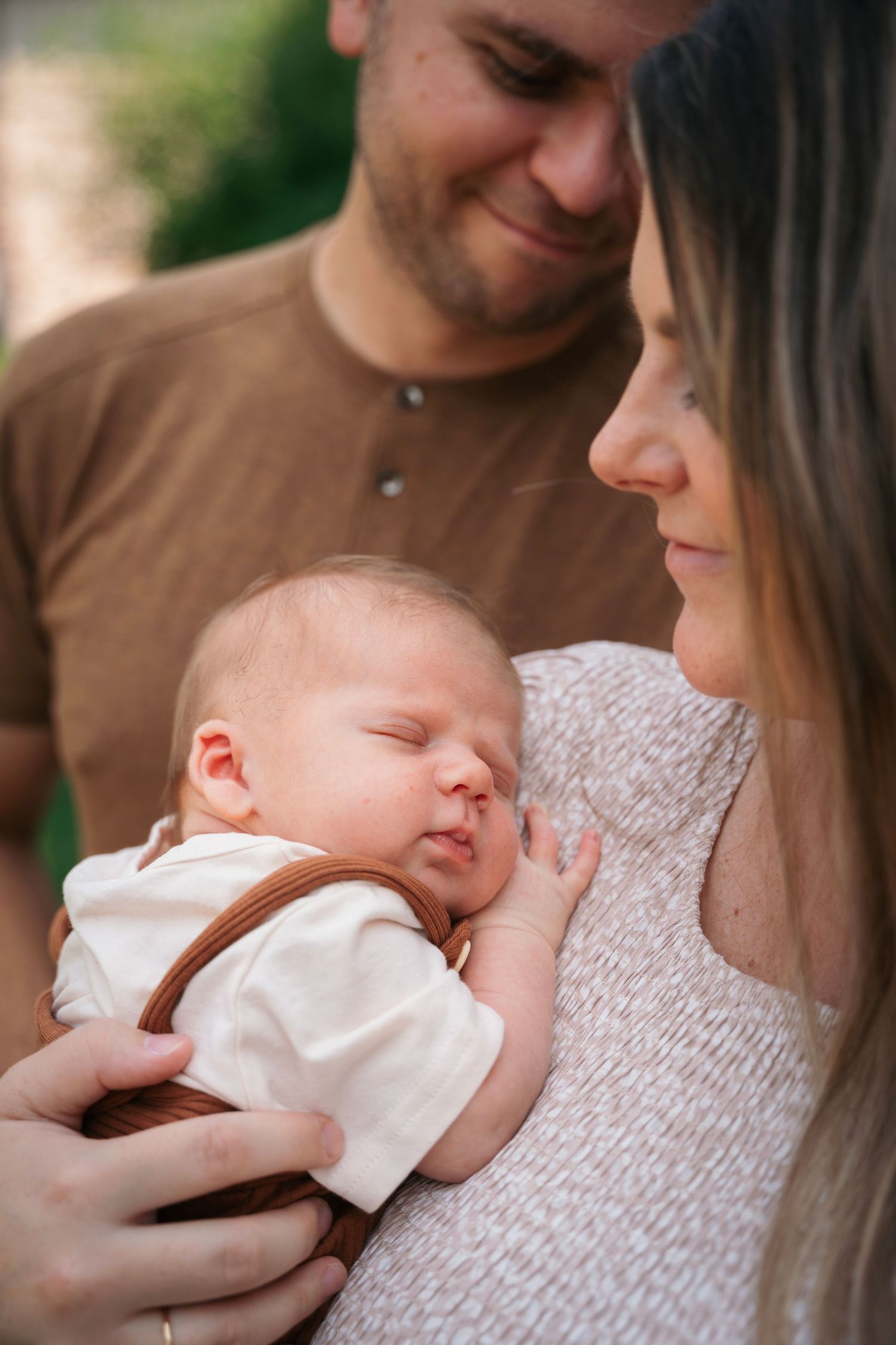 Tender family moment with sleeping newborn in white outfit.