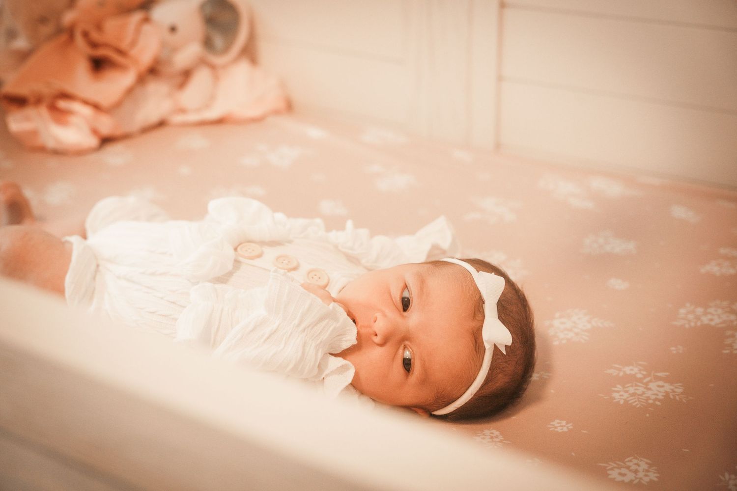 A baby lies on a soft pink blanket with a delicate white headband in Northbrook