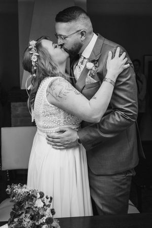 A black and white photo of the bride and groom sharing a romantic kiss at their wedding ceremony, the bride wearing a floral hair crown.
