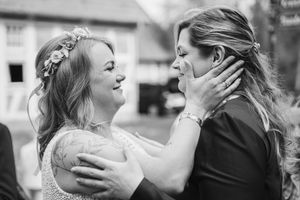 Black and white photo of a bride with a floral hair crown sharing a tender, emotional moment with a woman wiping her tears.