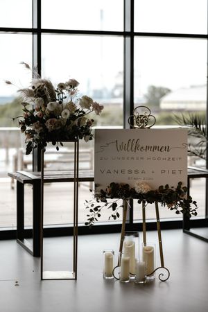 Elegant wedding welcome sign for Vanessa and Piet with candles and a floral arrangement beside large windows.