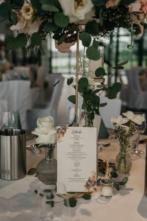 Festlich gedeckter Hochzeitstisch mit gedruckter Menükarte, weißen Rosen, Eukalyptus, Glasvasen und kleinen Kerzen. Lankenauer Höft Bremen