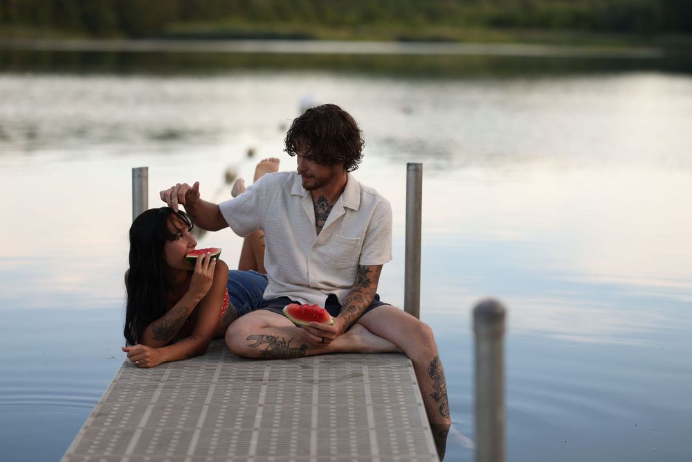 Couple relaxing on a wooden dock by a calm lake at sunset, sharing snacks and enjoying a romantic moment.