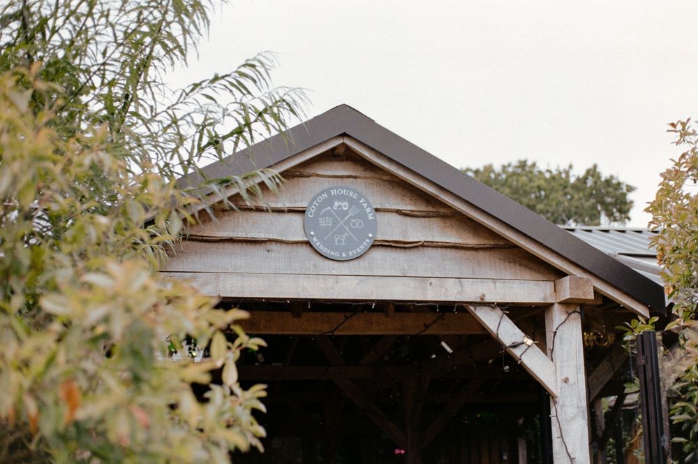Rustic wooden covered bridge entrance with decorative circular emblem, surrounded by lush green trees.