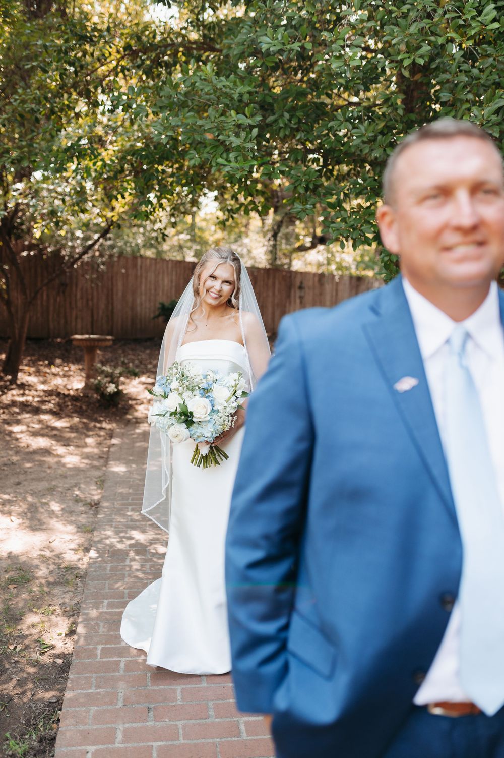 Bride in white gown holds bouquet during first look moment with father in blue suit.