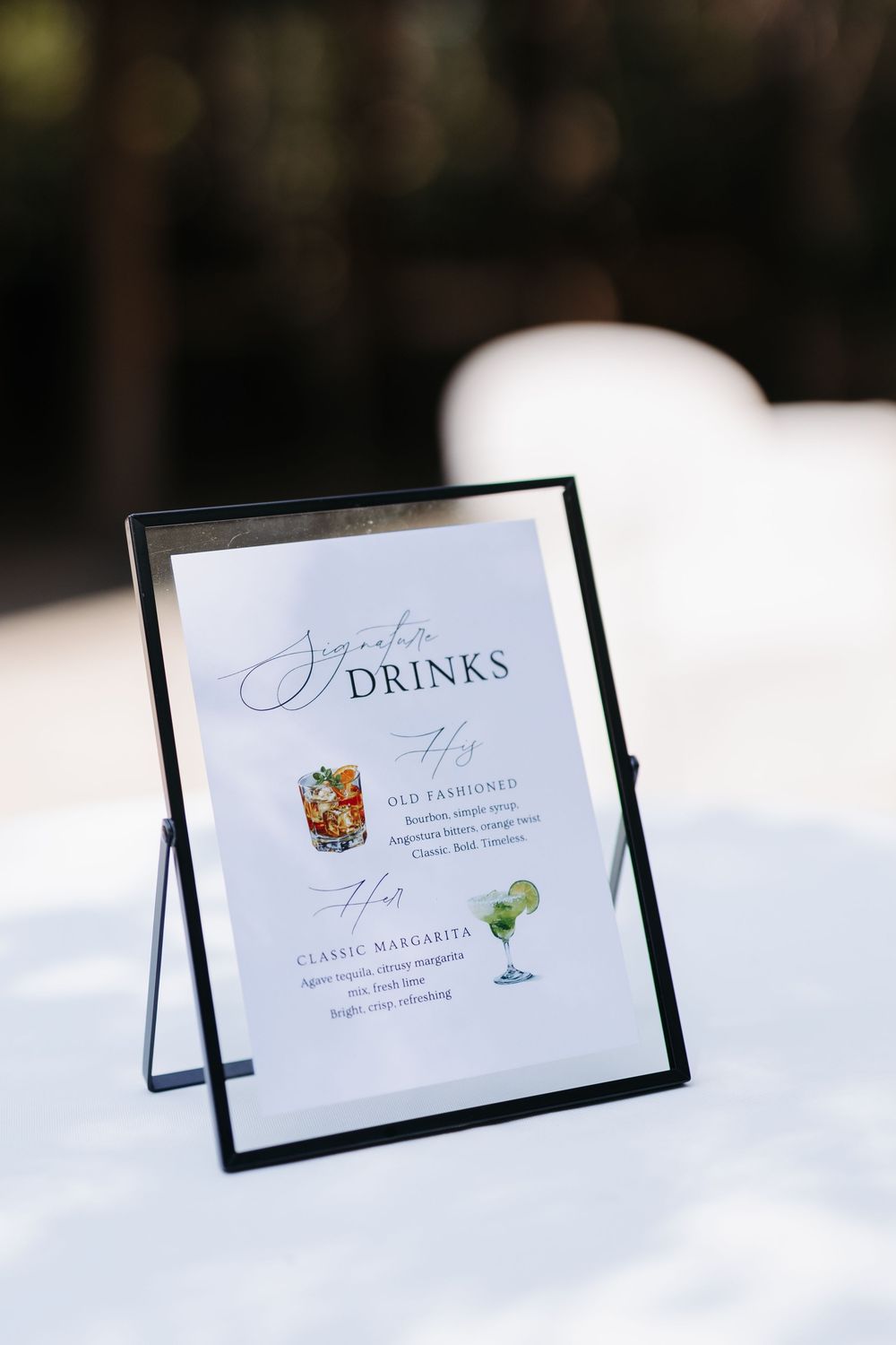 Elegant signature drinks menu in black frame displaying Old Fashioned and Classic Margarita cocktails at a wedding reception.