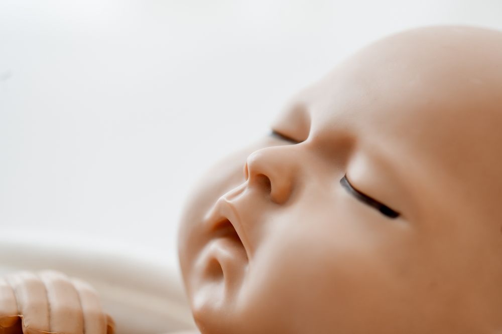 Peaceful sleeping newborn baby with closed eyes and delicate features resting on a white blanket.