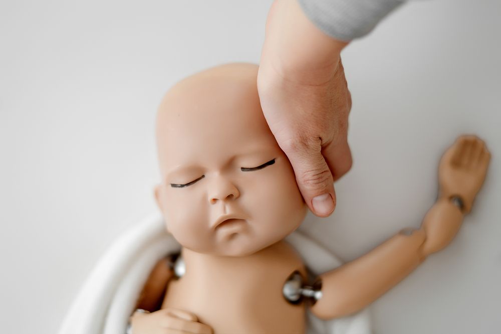 A hand gently touching the head of a realistic reborn baby doll with closed eyes and jointed limbs.