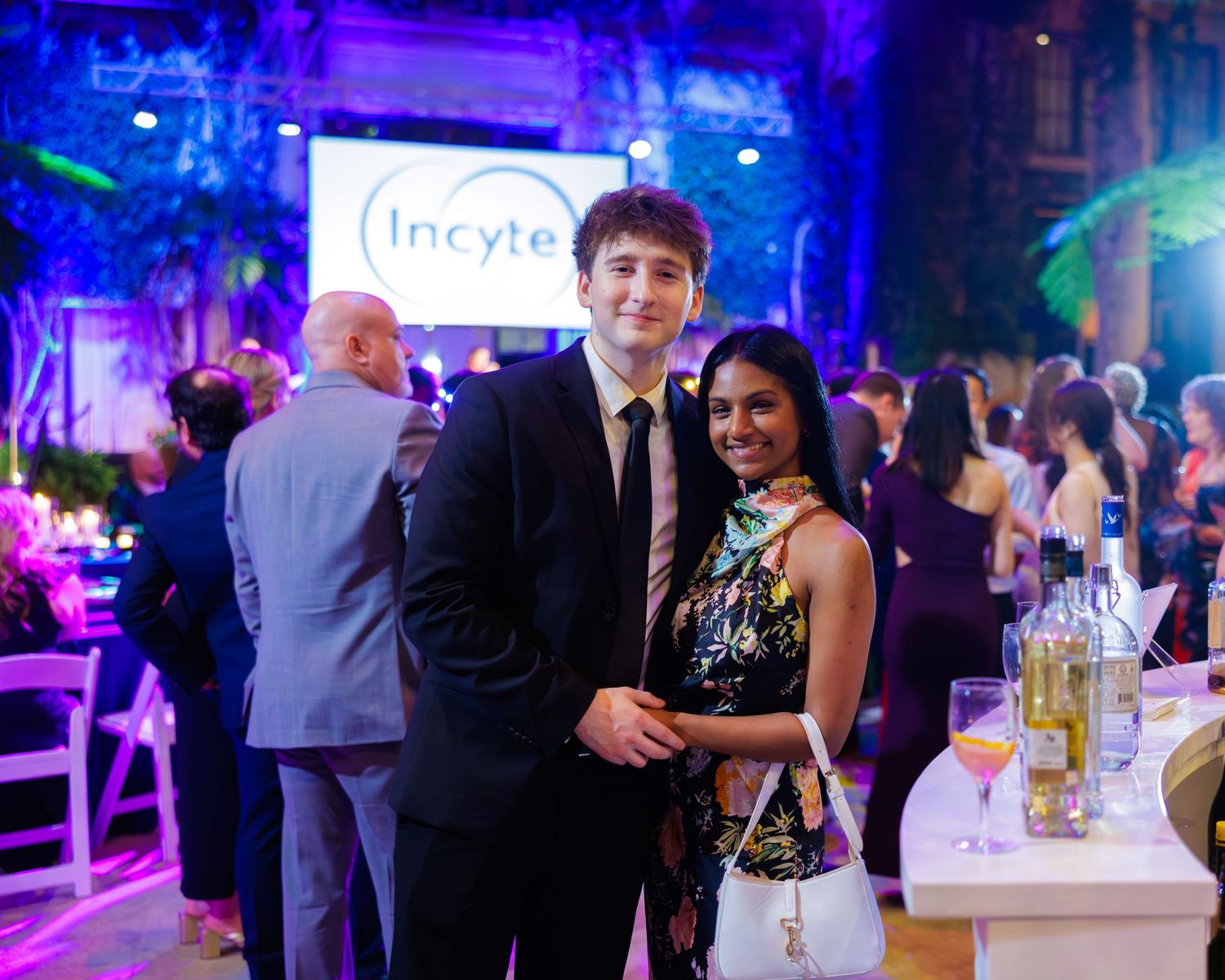 Couple posing at an Incyte corporate gala event with elegant purple lighting and guests in formal attire.