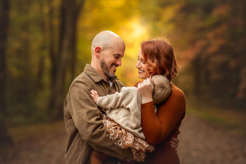 Couple embracing and smiling at each other on a forest path surrounded by golden autumn foliage.