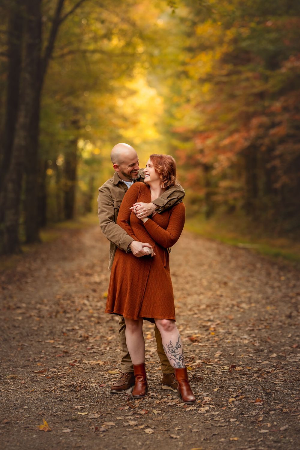 Couple embracing on a leaf-covered path surrounded by colorful autumn foliage.