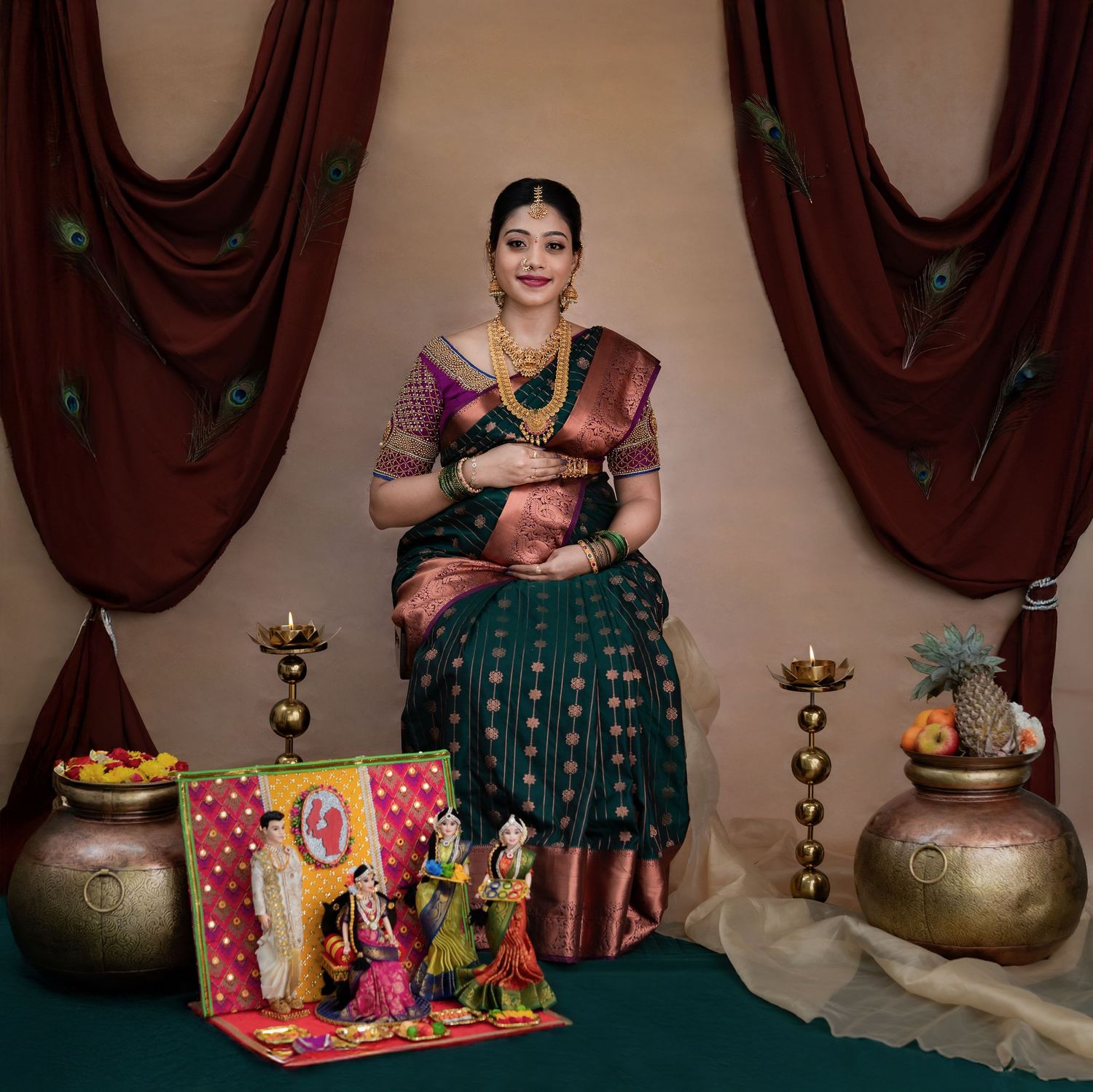 Expecting mother in a dark green and copper silk saree seated for a formal Seemantham-style portrait with ceremonial decor and brass pots