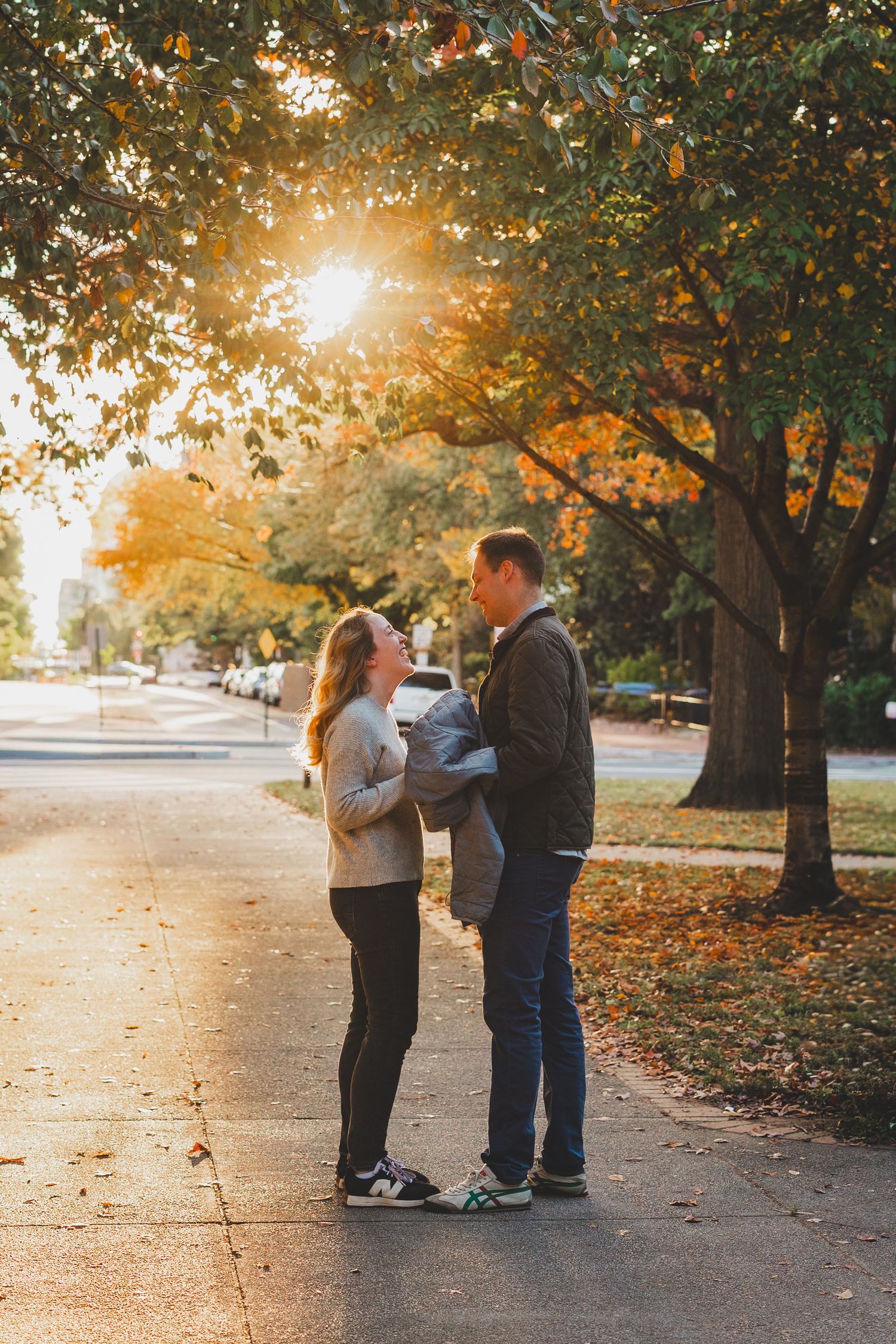 Couple sharing a tender moment on a tree-lined sidewalk in golden autumn sunlight moments before a surprise proposal in DC